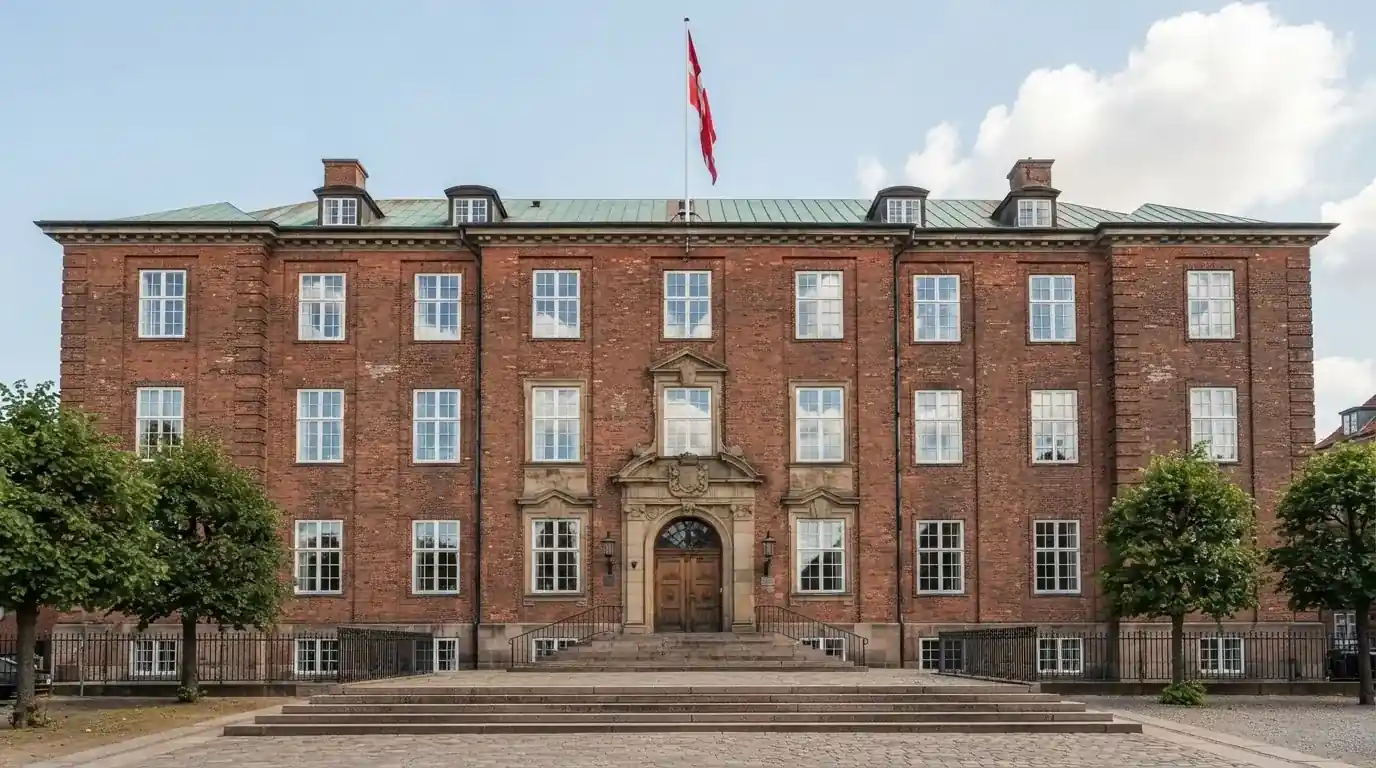 Facade af en klassisk dansk administrationsbygning i røde mursten med flagstang under blå himmel, uden personer.